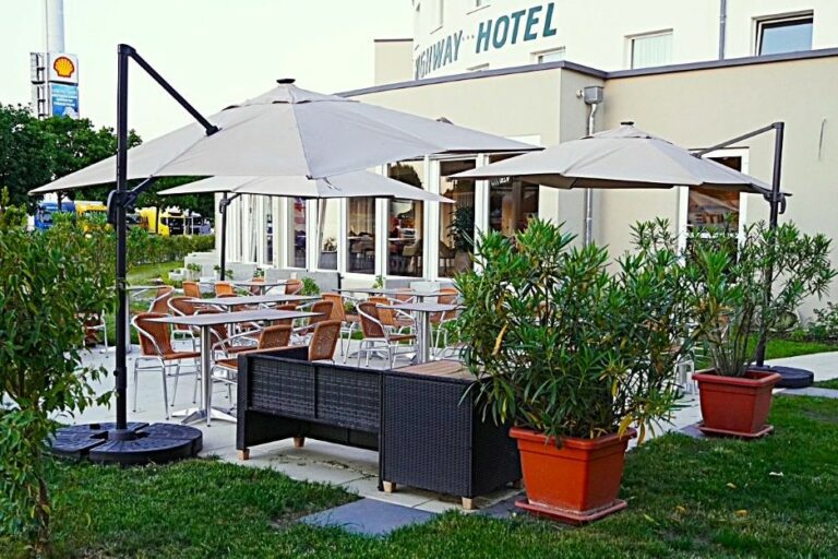 Gemütliche Terrasse des Highway Hotels mit Tischen, Stühlen, großen Sonnenschirmen und Blick auf das Hotelgebäude.