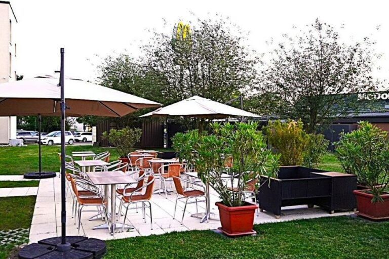 Sonnige Außenterrasse des Highway Hotels mit Sitzgelegenheiten, Sonnenschirmen und gepflegter Gartenanlage.
